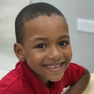 A small child wearing a red shirt smiles.