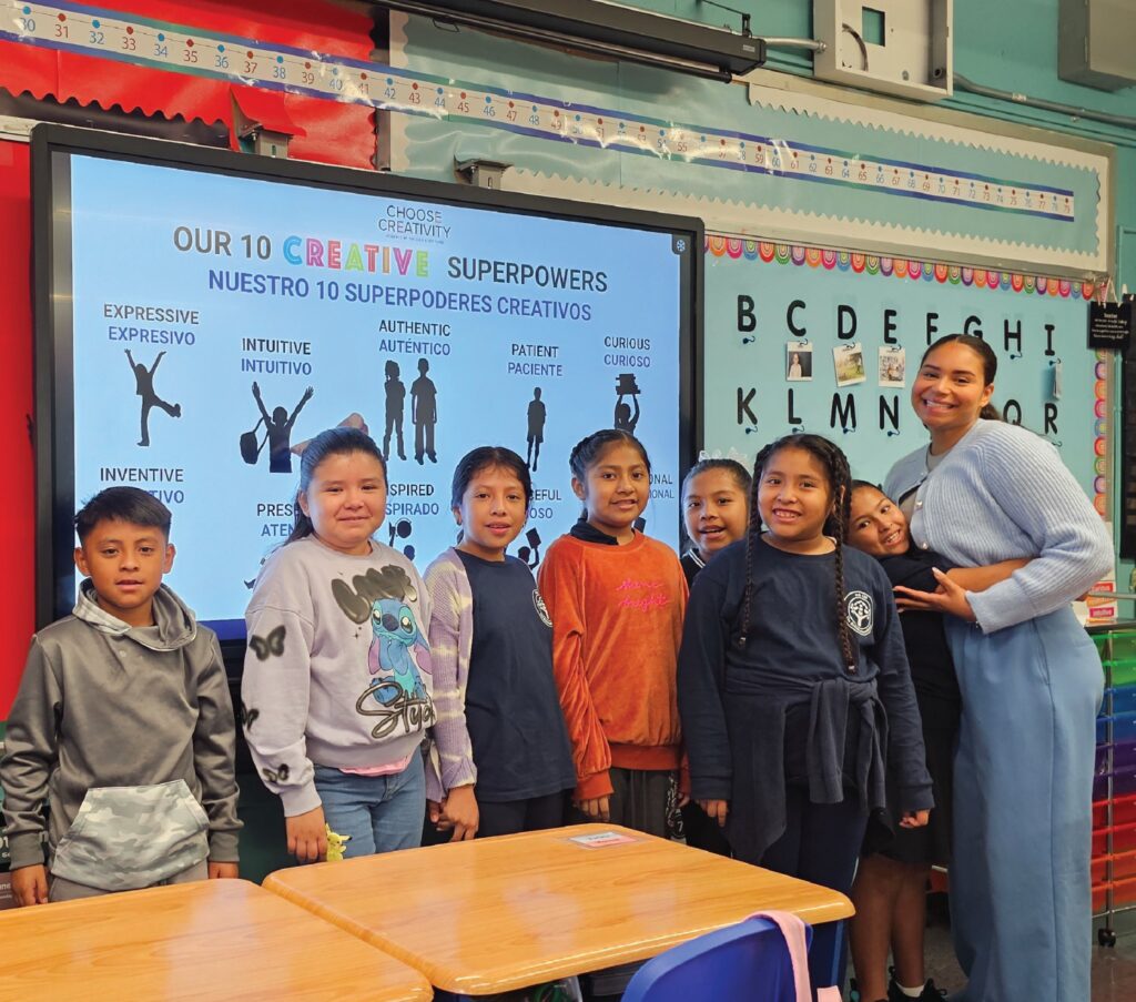 A teacher and her students beside a screen reading Our 10 Creative Superpowers in English and Spanish